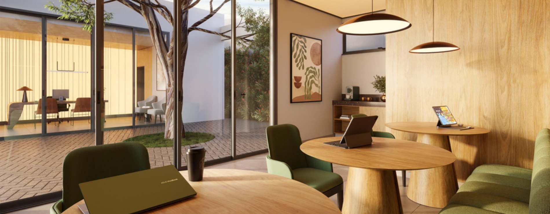 Espaço de coworking com mesas de madeira, poltronas verdes e jardim interno