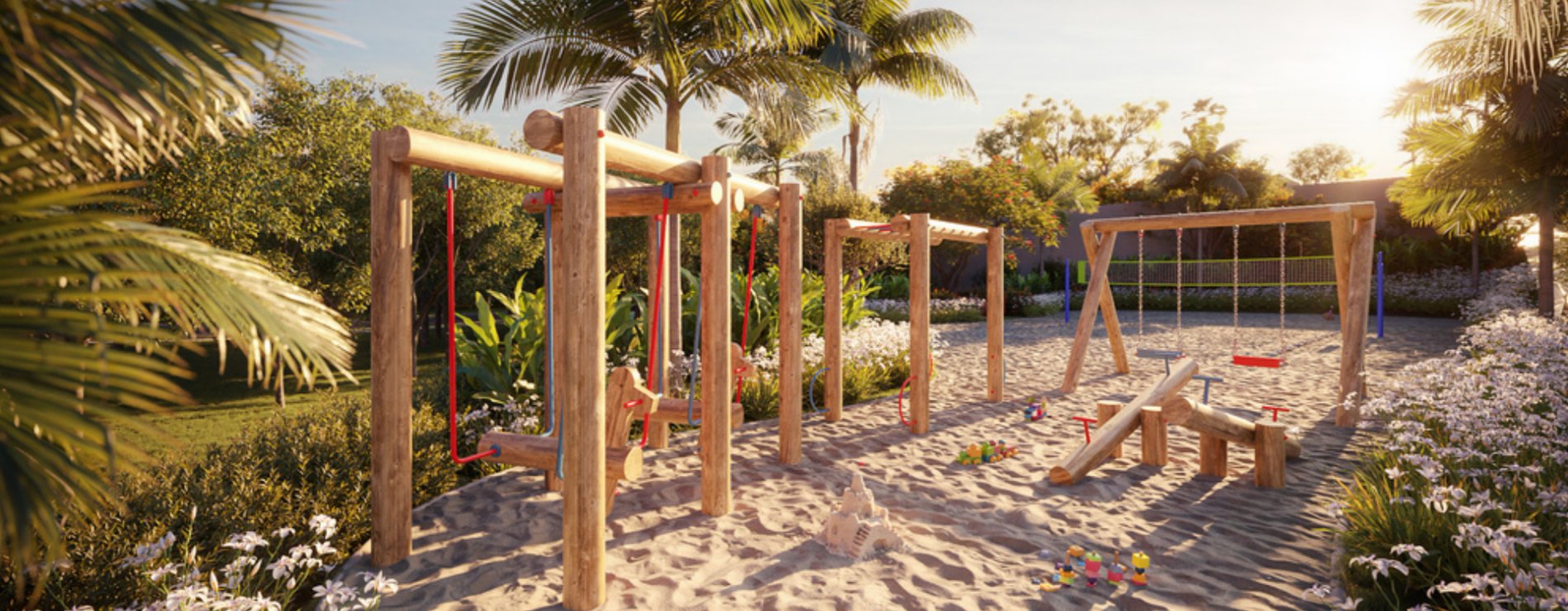 Playground de madeira sobre areia, cercado de palmeiras e flores
